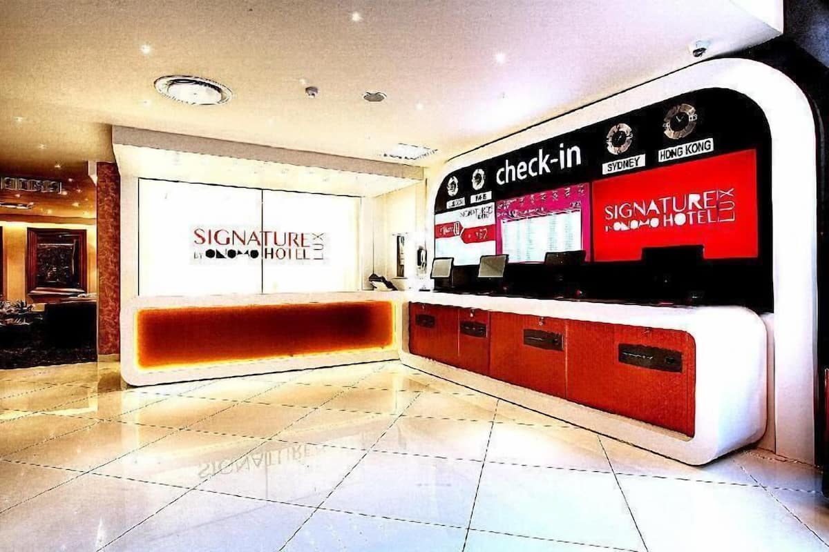 Un espace d’accueil d’hôtel comprenant un comptoir d’enregistrement, une grande enseigne indiquant « Signature Hotel », et un écran numérique affichant les différents emplacements de l’hôtel.