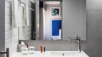 Un baño moderno con un lavamanos blanco, dos toallas, un espejo y una obra de arte enmarcada en la pared.