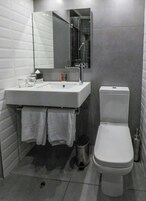 Un baño moderno con un lavamanos blanco, un inodoro y un espejo sobre el lavamanos.