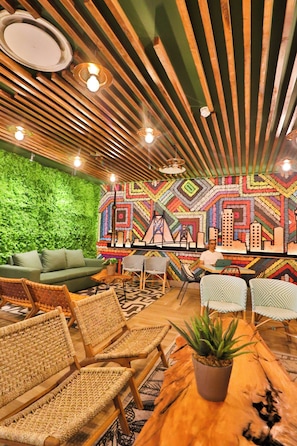 Una habitación con pared verde, muebles de fibras tejidas y un colorido mural geométrico.