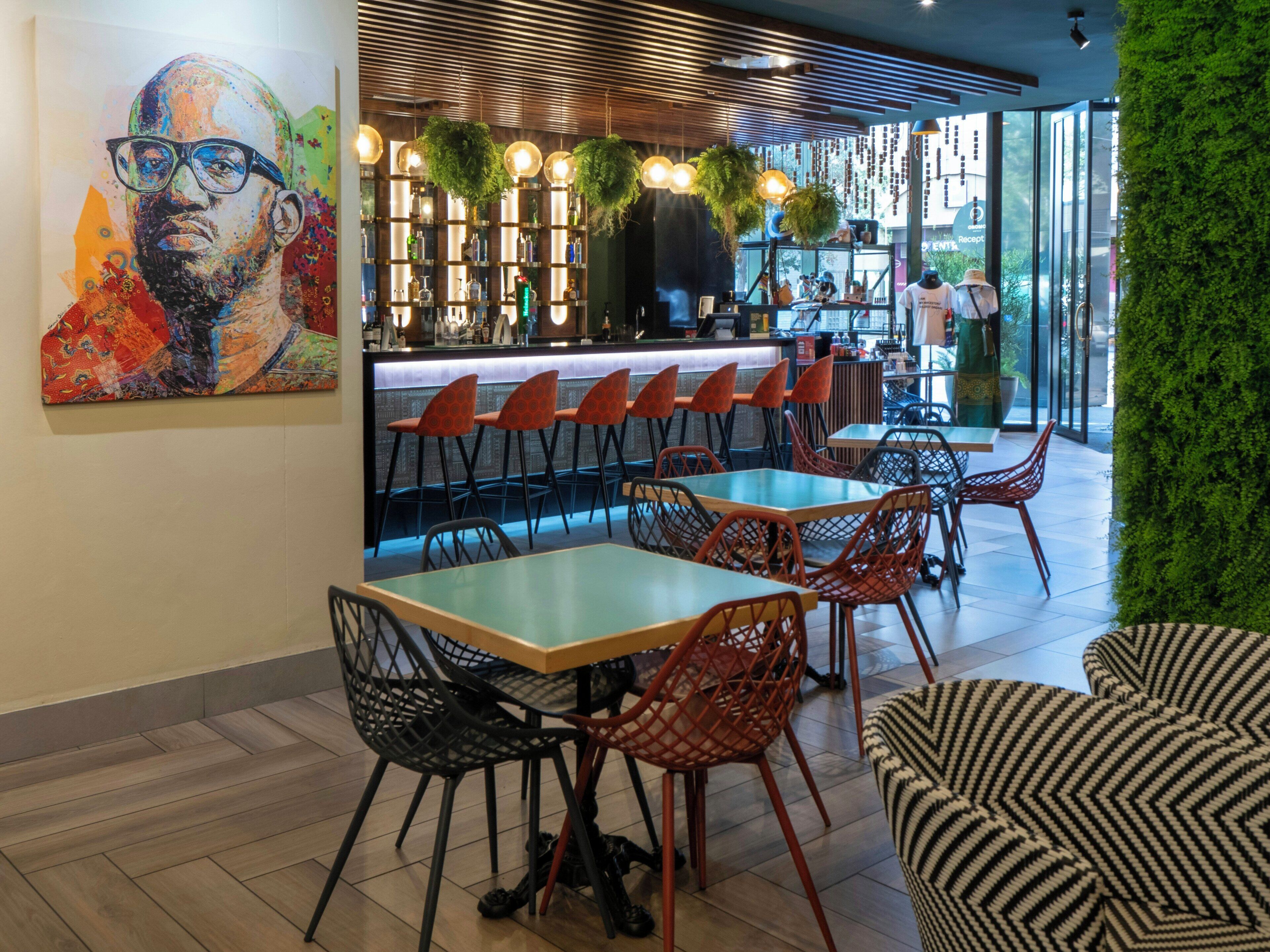 A modern restaurant interior with bar seating, a green wall, and a large painting on the wall.