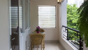 A narrow balcony with a table and chairs, a window with blinds, and a view of greenery outside. - Thao Nguyen Apartment (Ho Chi Minh City)