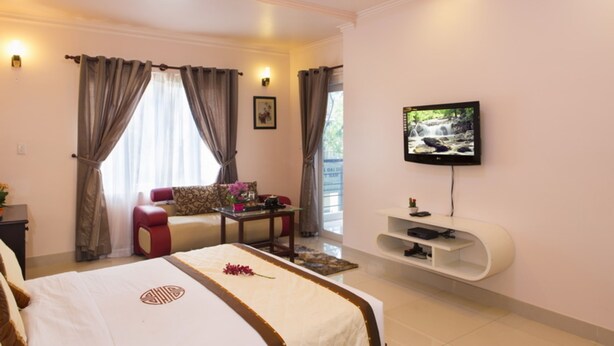 A hotel room with a bed, a sofa, a TV, and a small table. - Thao Nguyen Apartment (Ho Chi Minh City)