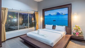 Een hotelkamer met een groot bed, een aan de muur bevestigde televisie, een raam met gordijnen en een kleine tafel met een bloevas.