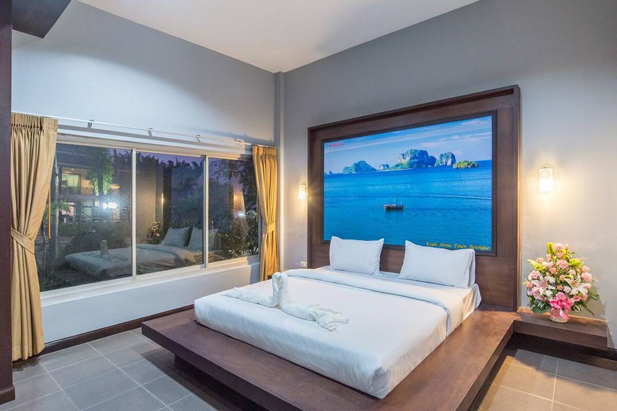 Une chambre d’hôtel avec un grand lit, un téléviseur fixé au mur, une fenêtre avec des rideaux et une petite table sur laquelle est posé un vase de fleurs.