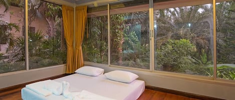 Una habitación de hotel con una cama grande, una ventana con cortinas y vistas a vegetación tropical.