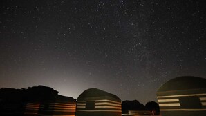 A starry night sky with three dome-shaped structures, each with horizontal stripes, under a clear sky. - Wadi Rum Sky (Wadi Rum)