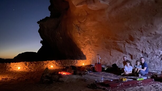A cave interior with a fire, a red suitcase, and a group of people. - Wadi Rum Sky (Wadi Rum)