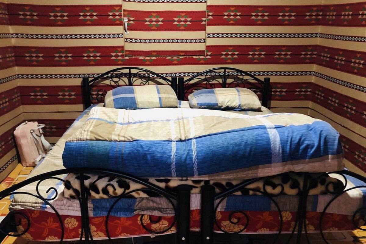 A bed with a patterned bedspread and pillows, a metal headboard, and a wall with a geometric patterned tapestry.