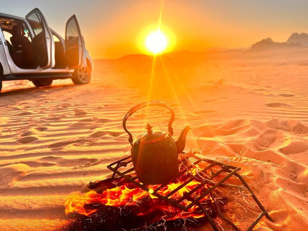 A desert scene with a car and a campfire with a kettle.