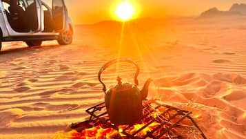 A desert scene with a car and a campfire with a kettle.