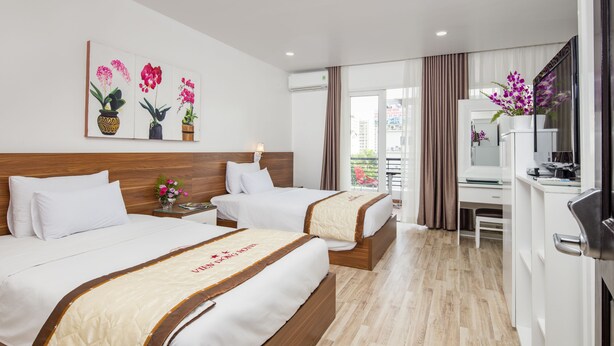 Habitación de hotel con dos camas, un escritorio, una silla y un ventanal con cortinas.