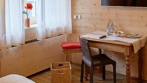 A cozy room with a wooden ceiling, a bed, a table with a chair, a TV mounted on the wall, and a window with curtains. - Hotel Capima (Cologne)