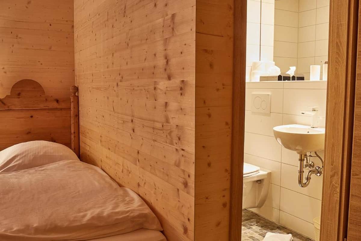 Ein Zimmer mit Holzboden, einem Bett und einem durchgehenden Türrahmen sichtbaren Badezimmer.