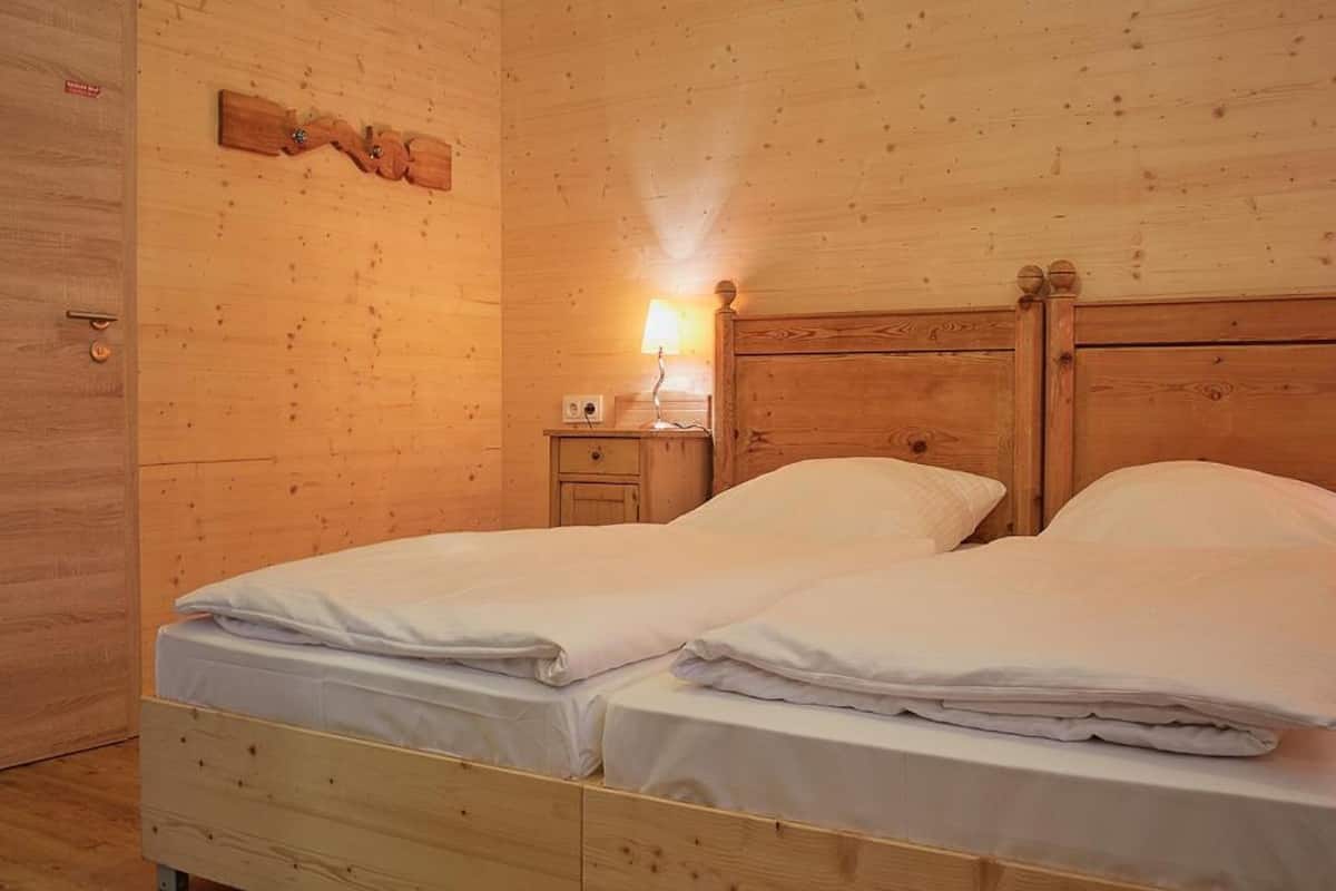 Ein Zimmer mit Holzboden, zwei Betten, einem Nachttisch mit Lampe und einer Holzdeko an der Wand.