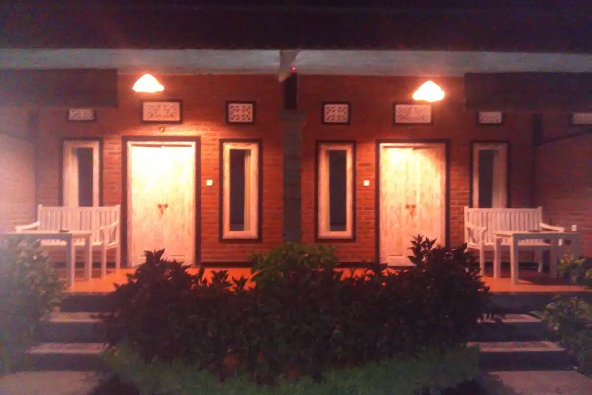 Um edifício com duas portas, cada uma com uma pequena janela acima. Há duas cadeiras brancas em frente a cada porta.