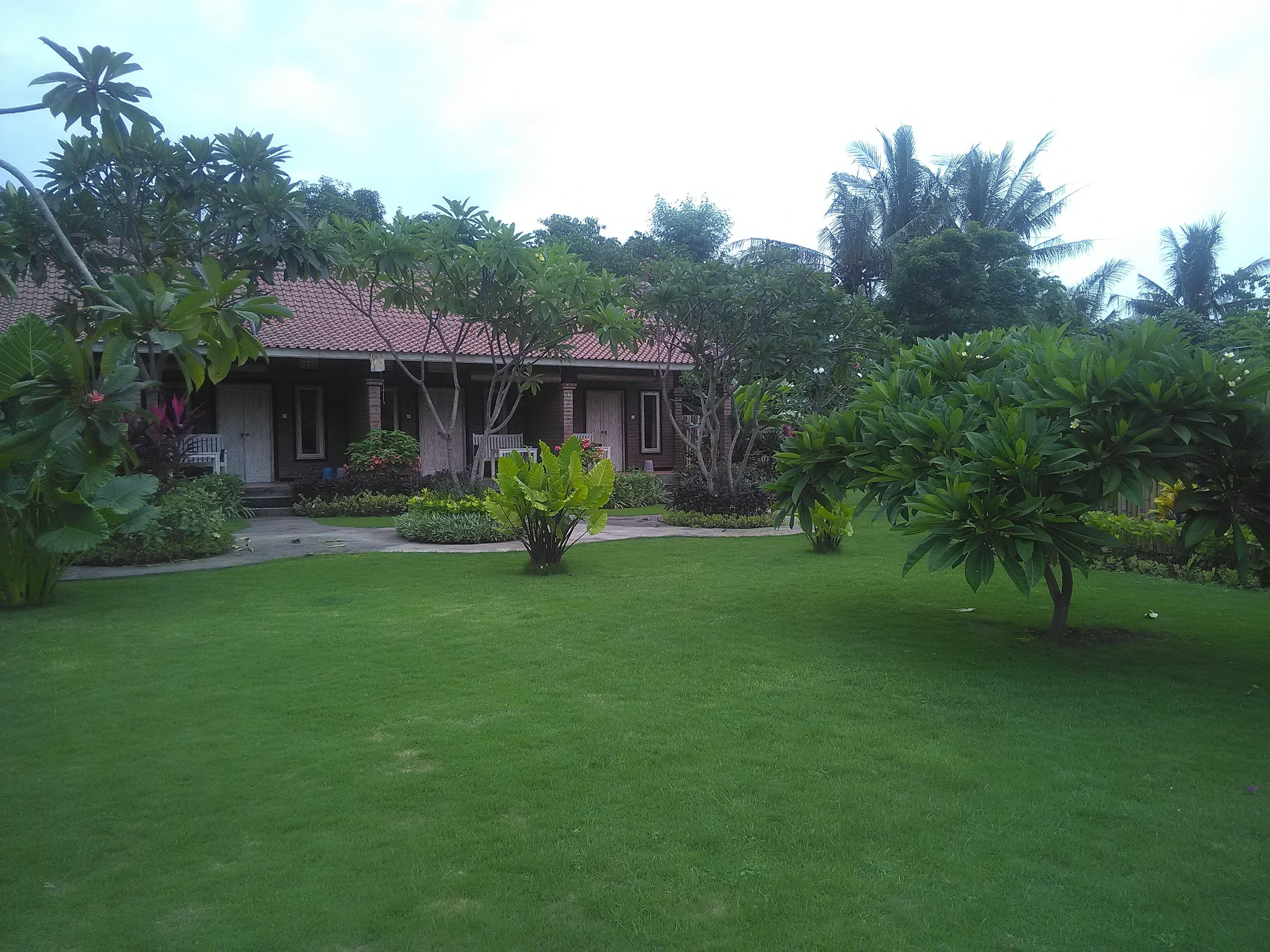 A house with a red-tiled roof, surrounded by lush greenery and a well-maintained lawn.