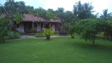 A house with a red-tiled roof, surrounded by lush greenery and a well-maintained lawn.