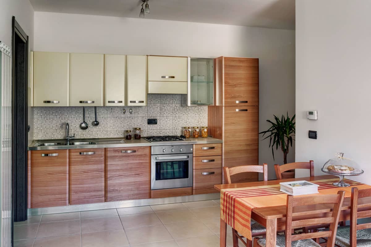 A modern kitchen with wooden cabinets, a tiled backsplash, and a dining area with a table and chairs.