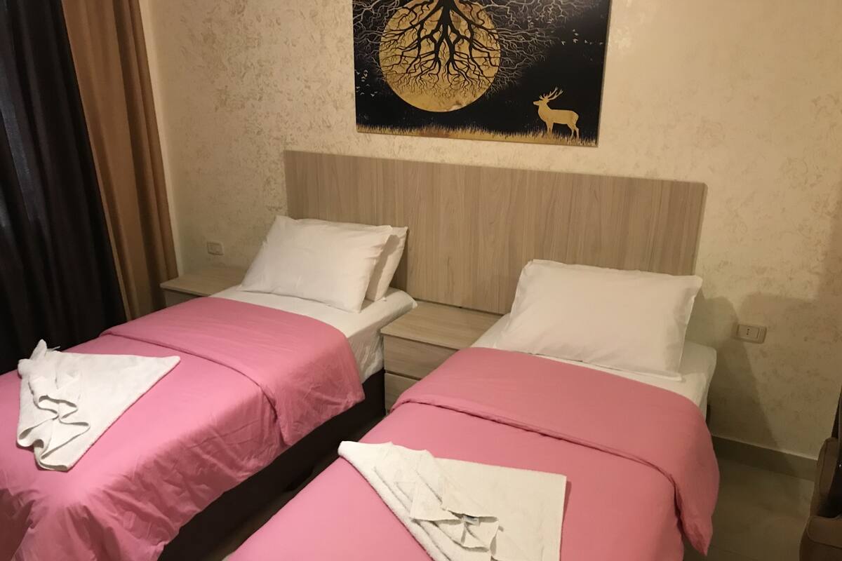 Two single beds with pink bedding and white pillows, a wooden headboard, and a wall-mounted artwork of a tree and deer.