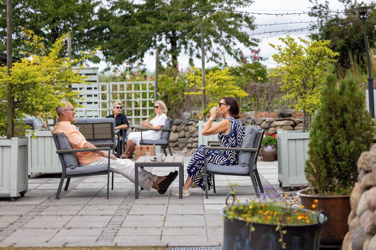 An outdoor seating area with four people seated on chairs, a table, and potted plants.