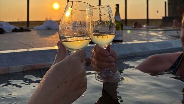 Dos personas brindando con copas de vino en una zona de piscina al atardecer.
