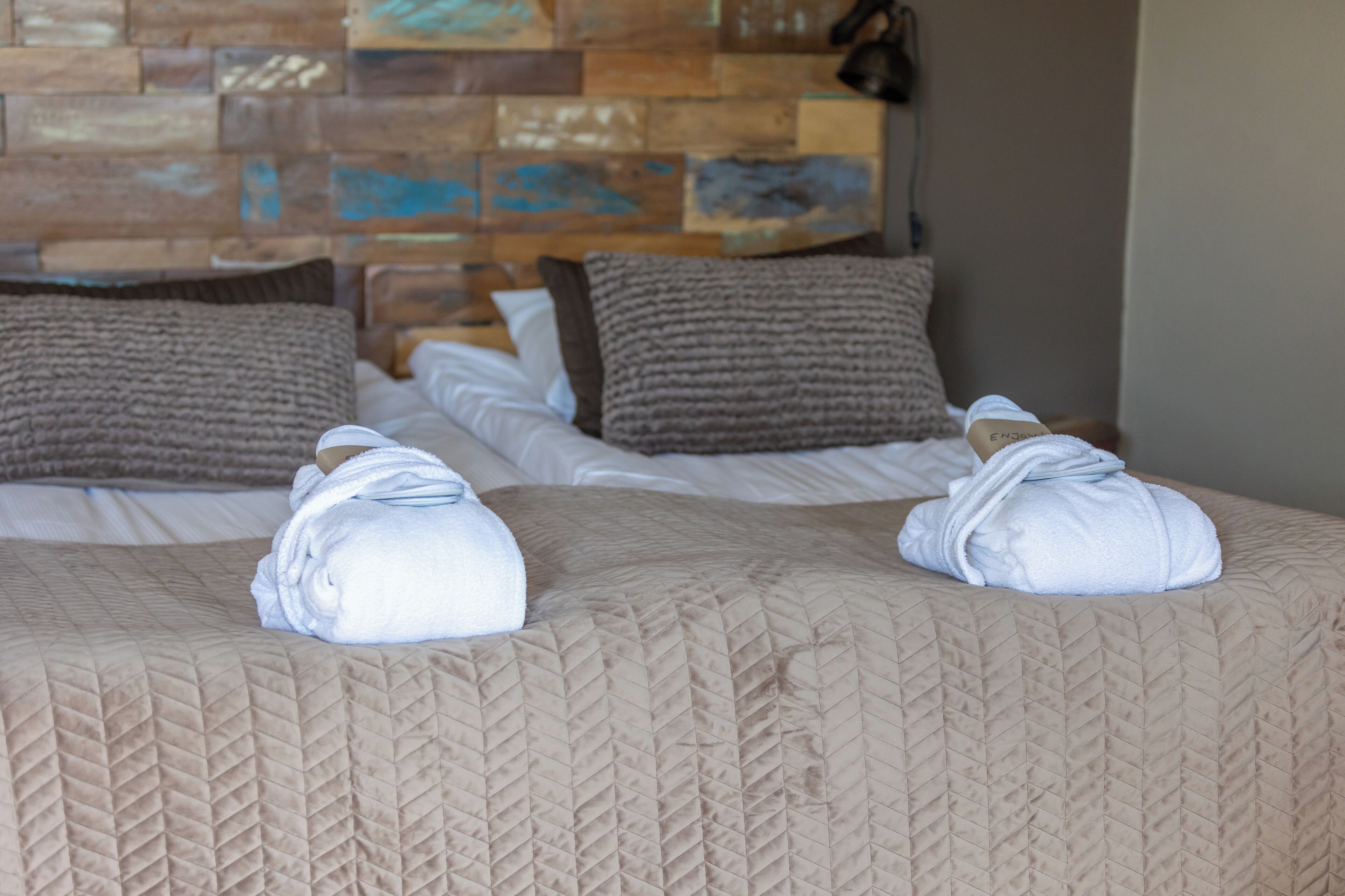 Ein Hotelzimmer mit zwei Betten, jeweils mit einer gesteppten, beige farbenen Tagesdecke und zwei braunen Kissen.
