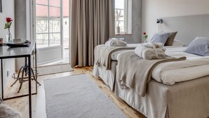 Habitación de hotel con dos camas, un escritorio, una silla, una ventana con cortinas y vistas al exterior.