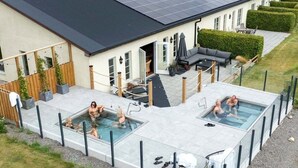 Edificio residencial con un sistema de paneles solares en la azotea, zona de piscina con paredes de vidrio y un patio cubierto con mobiliario exterior.