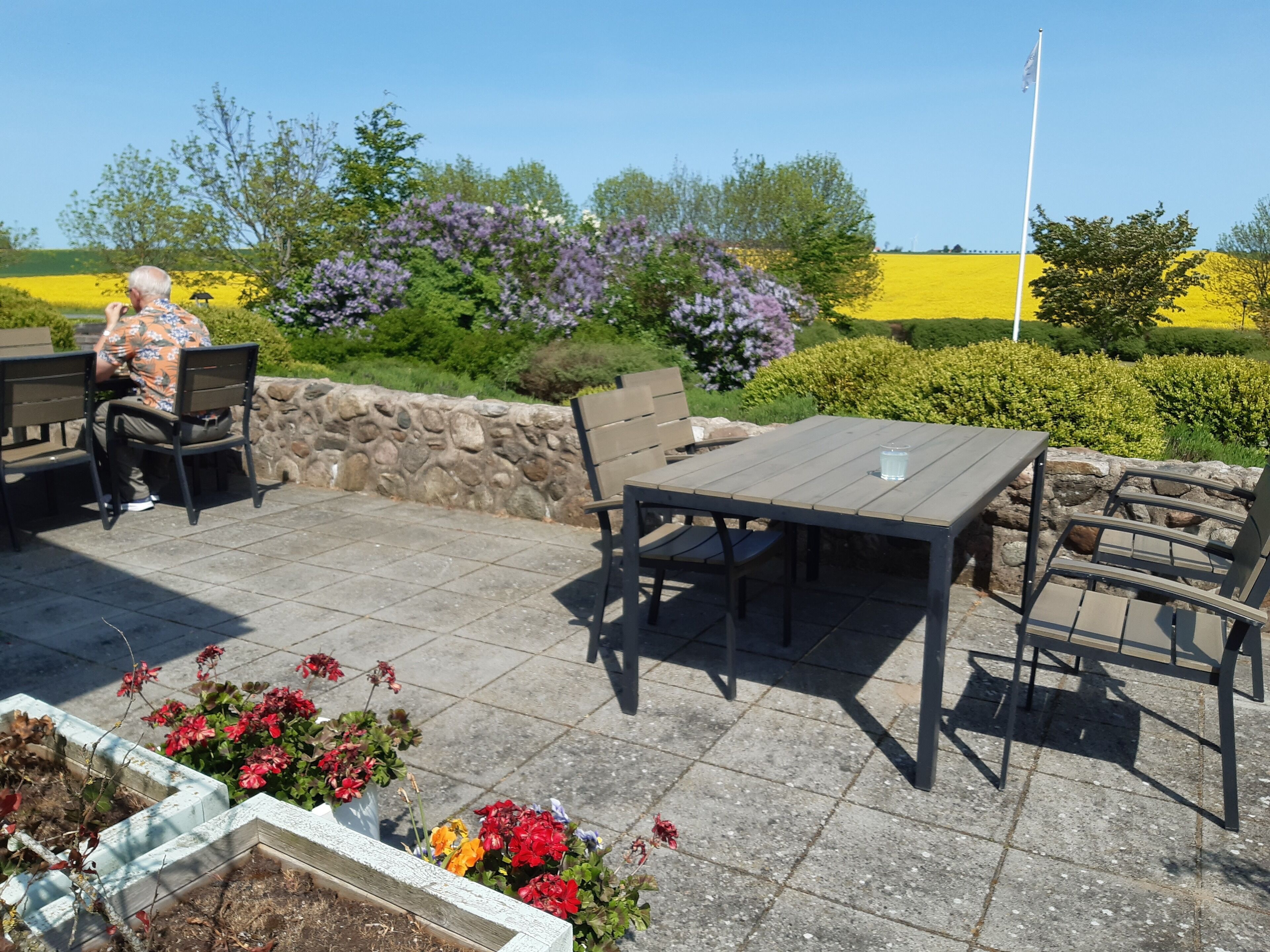 An outdoor patio area with stone flooring, a table, chairs, and a person seated.