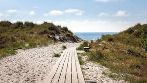 Un sendero arenoso que conduce al mar, con una pasarela de madera.