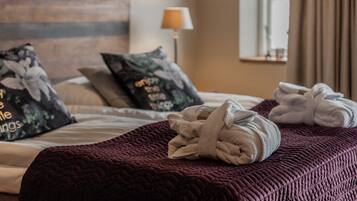 Una cama bien tendida con una colcha rojo oscuro, dos toallas y almohadones con motivos florales.