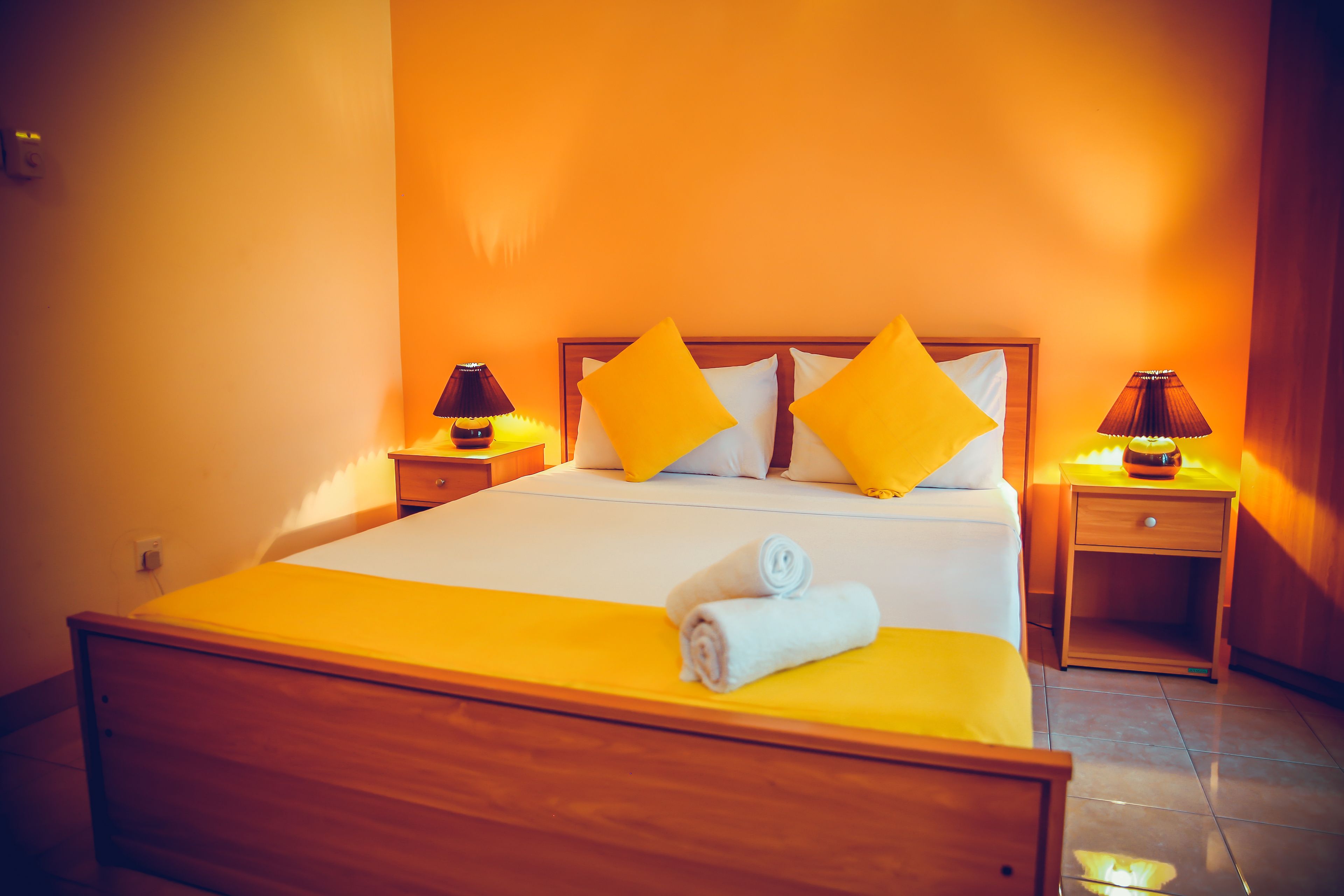 Una cama bien hecha con ropa de cama y almohadas amarillas, dos mesitas de noche con lámparas y un cabecero de madera.
