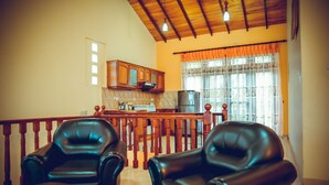 A living room with two leather chairs, a coffee table, and a kitchen area with wooden cabinets and a refrigerator. - The Terranova Inn (Negombo)