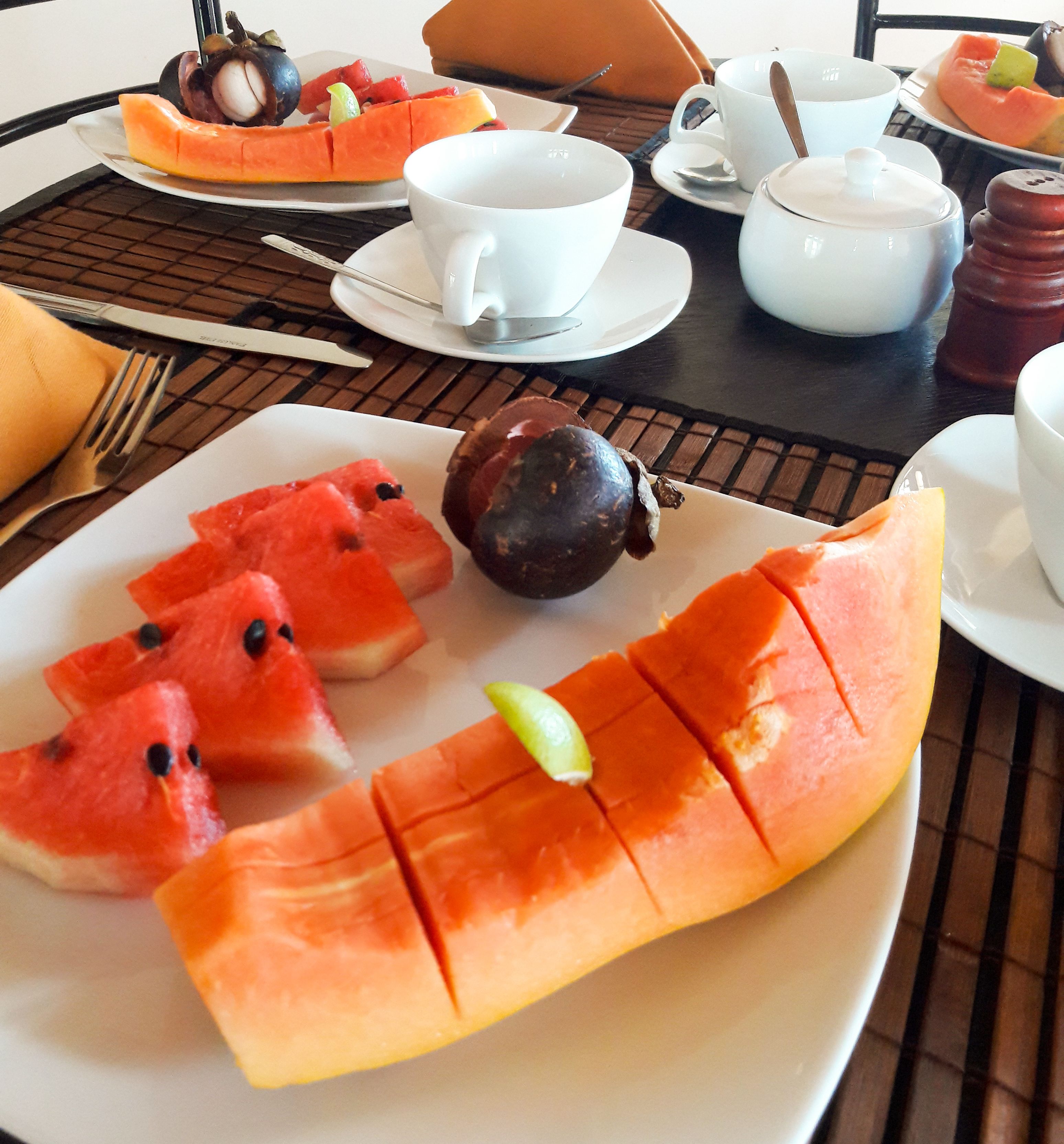 Una mesa con una fuente de sandía y melón, un tazón de sopa y una taza de té.