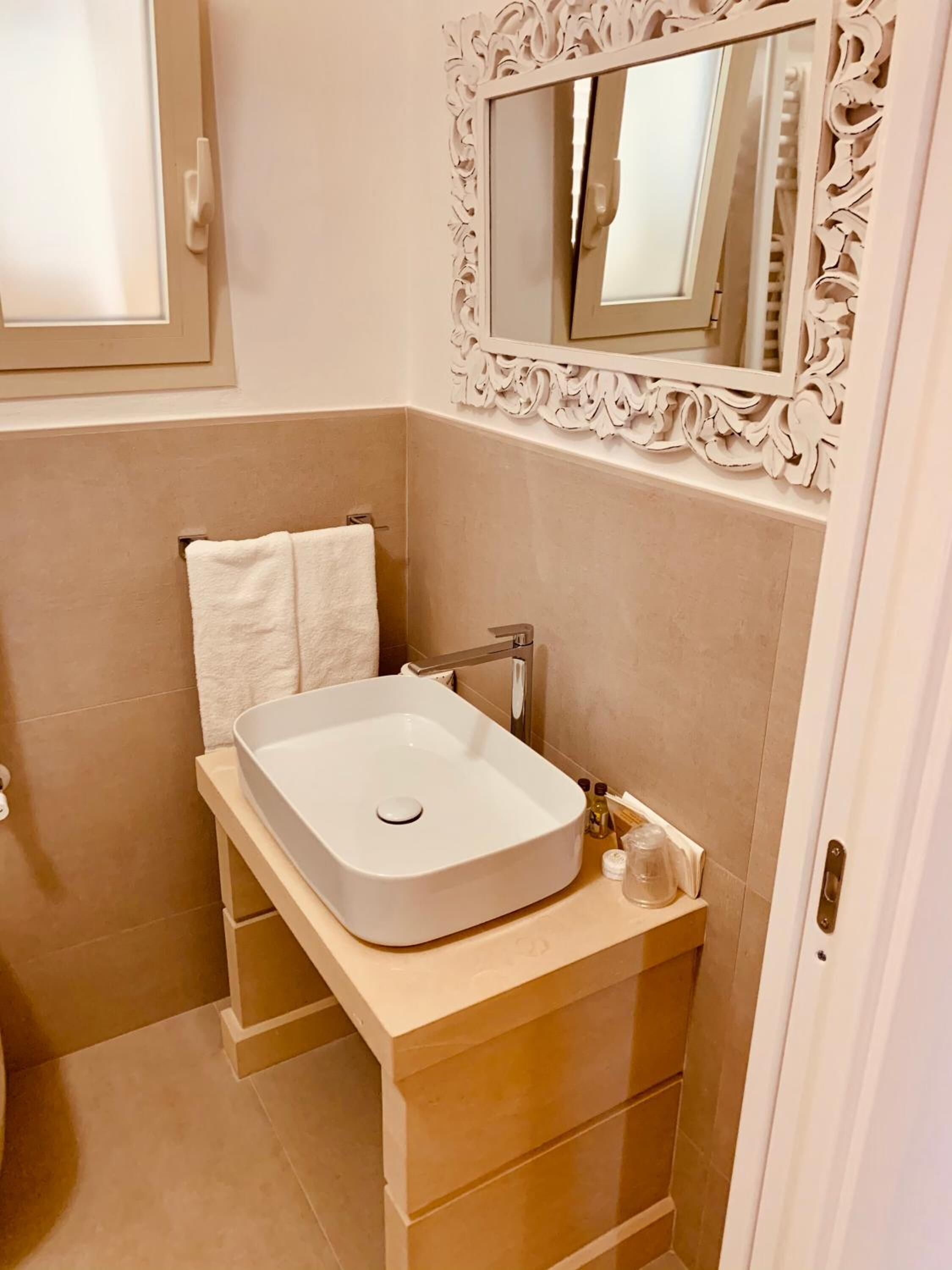 Une salle de bain avec un lavabo blanc, un miroir doté d’un cadre orné et une serviette accrochée au mur.