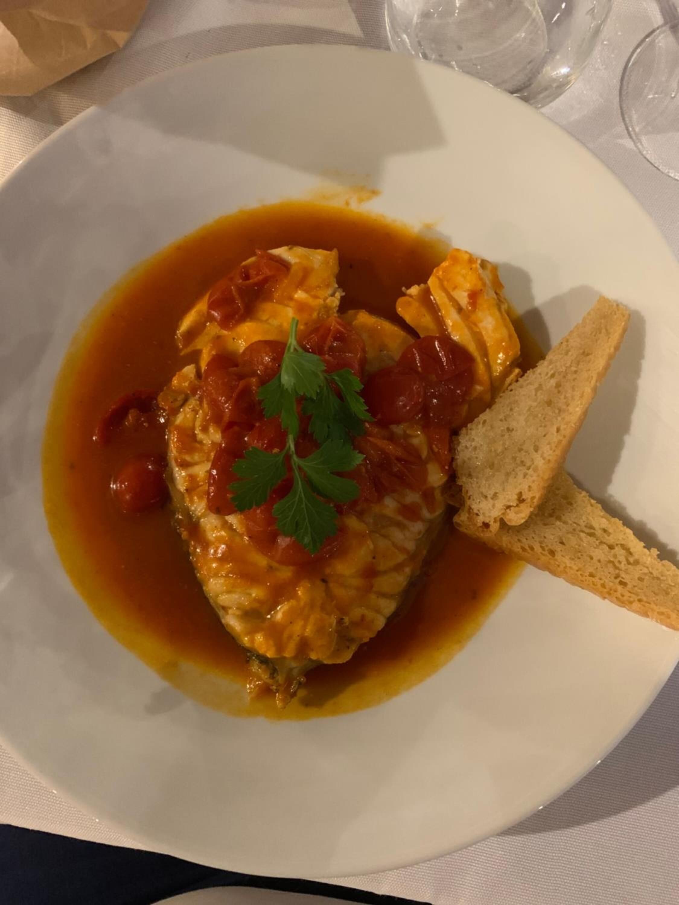 A plate with a dish of chicken in tomato sauce, garnished with parsley, and accompanied by a slice of bread.