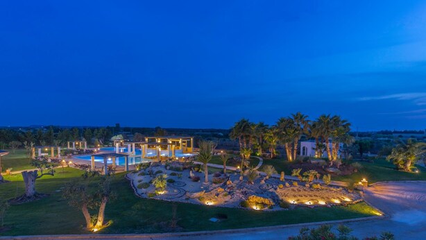 Un resort con piscina, palmeras y un área exterior bien iluminada al anochecer.