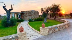 Un edificio de piedra con diseño circular, rodeado por un muro de piedra y un camino pavimentado.