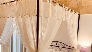 Una cama con dosel, cortinas blancas, una mesita de noche con lámpara y vistas a un muro de piedra.