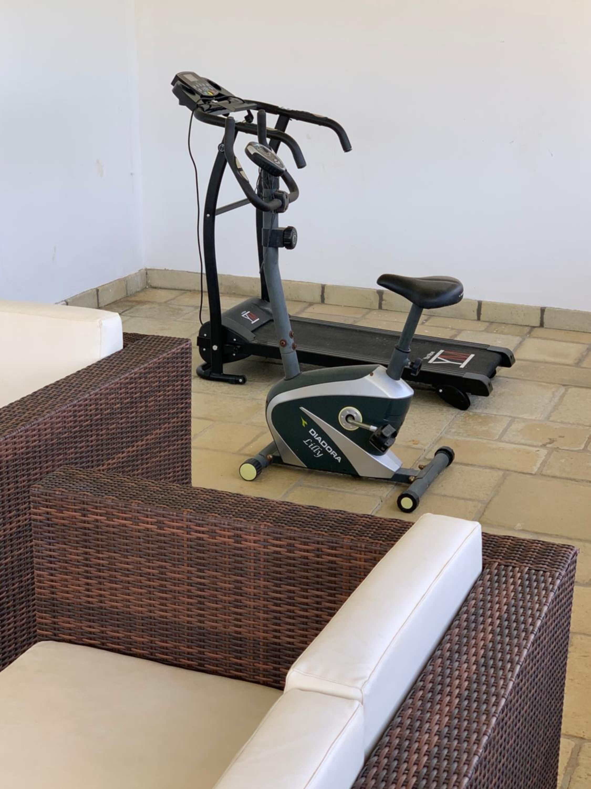 Ein Zimmer mit einem Crosstrainer, Korbmöbeln und Fliesenboden.