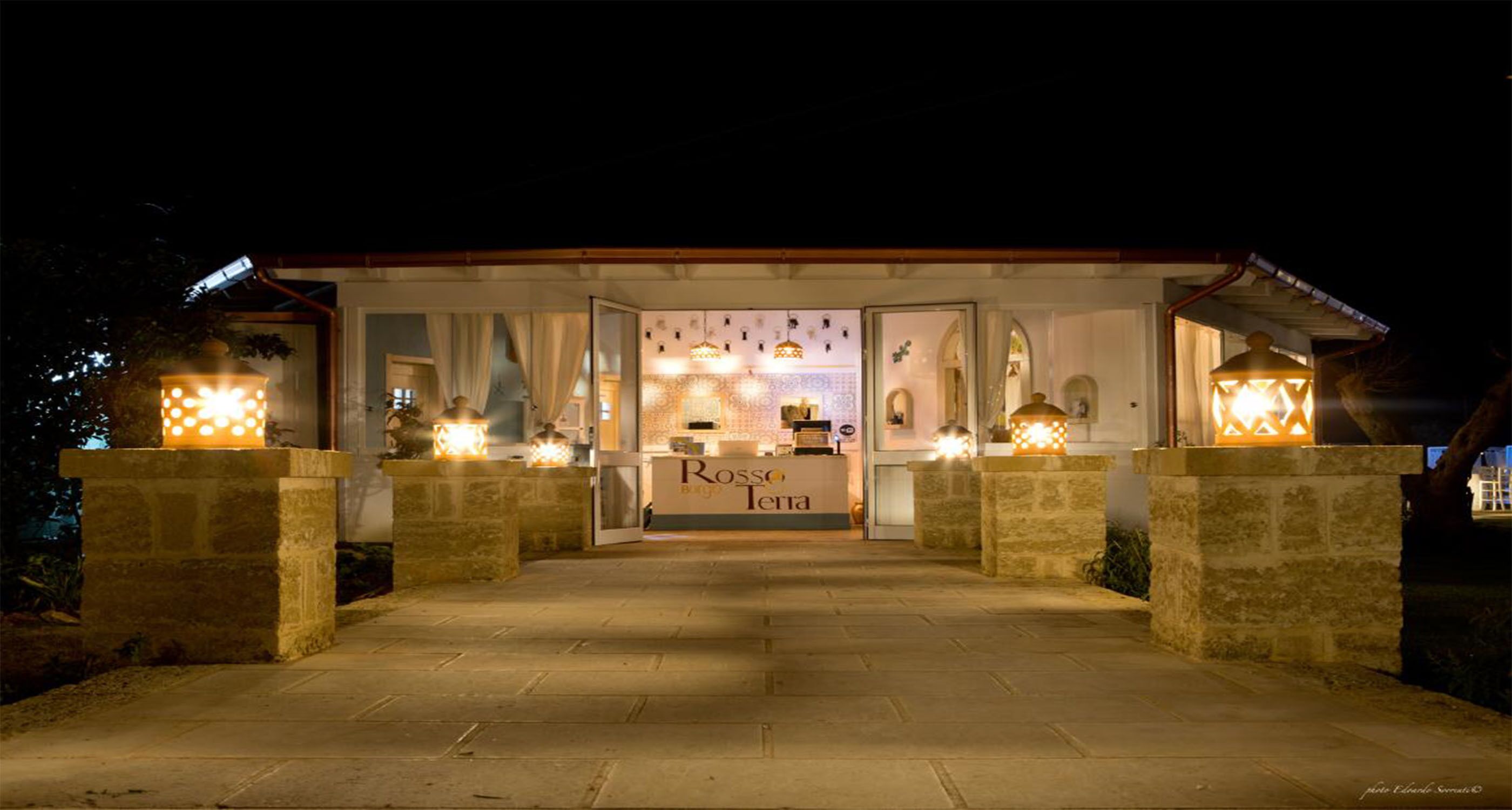 Un restaurante acogedor y bien iluminado llamado "Rosso Terra", con fachada de piedra, luz cálida y una entrada atractiva.