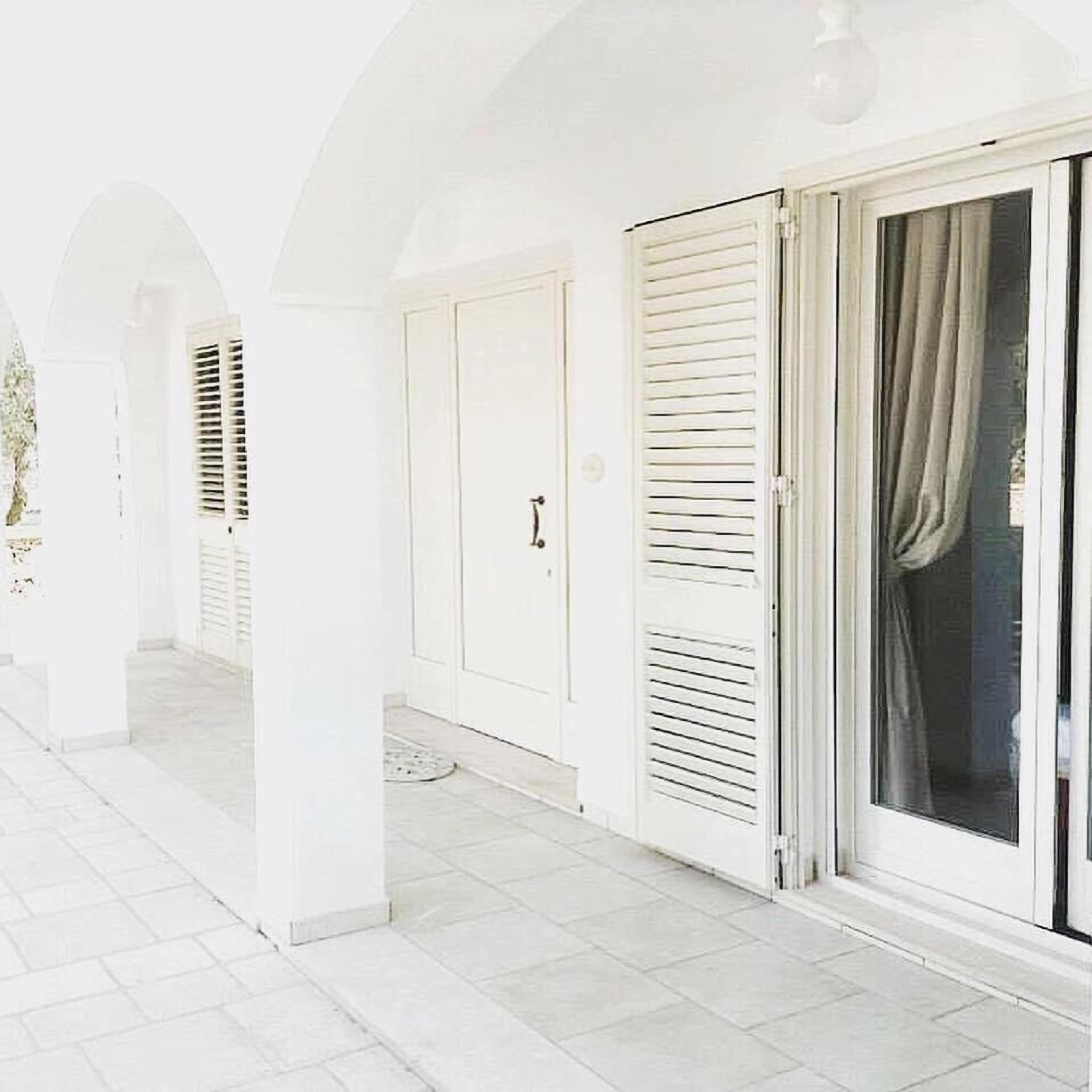 A white corridor with a tiled floor, a door with a handle, and a sliding glass door with a curtain.