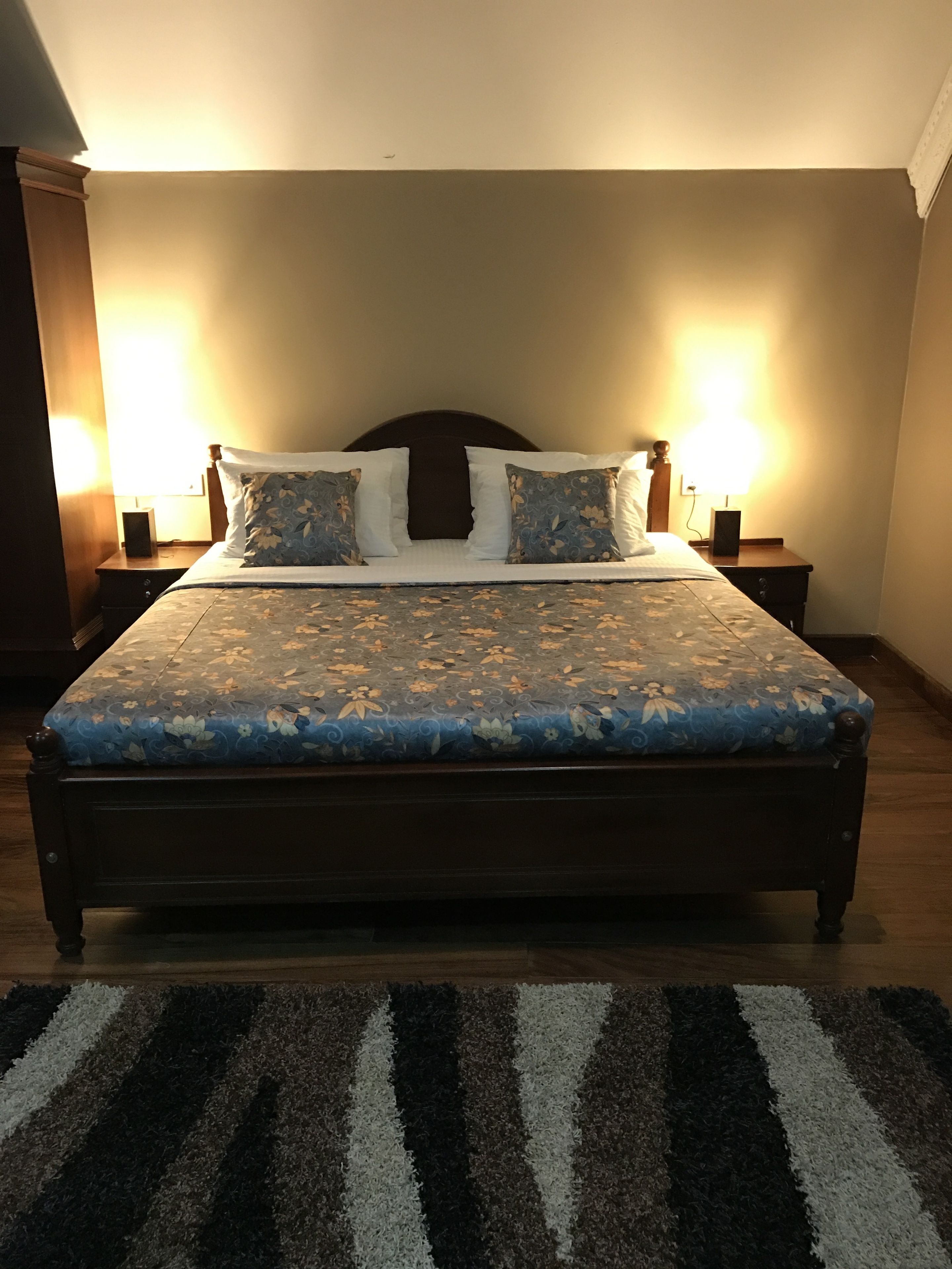 A bed with floral bedding, two bedside lamps, and a striped rug.