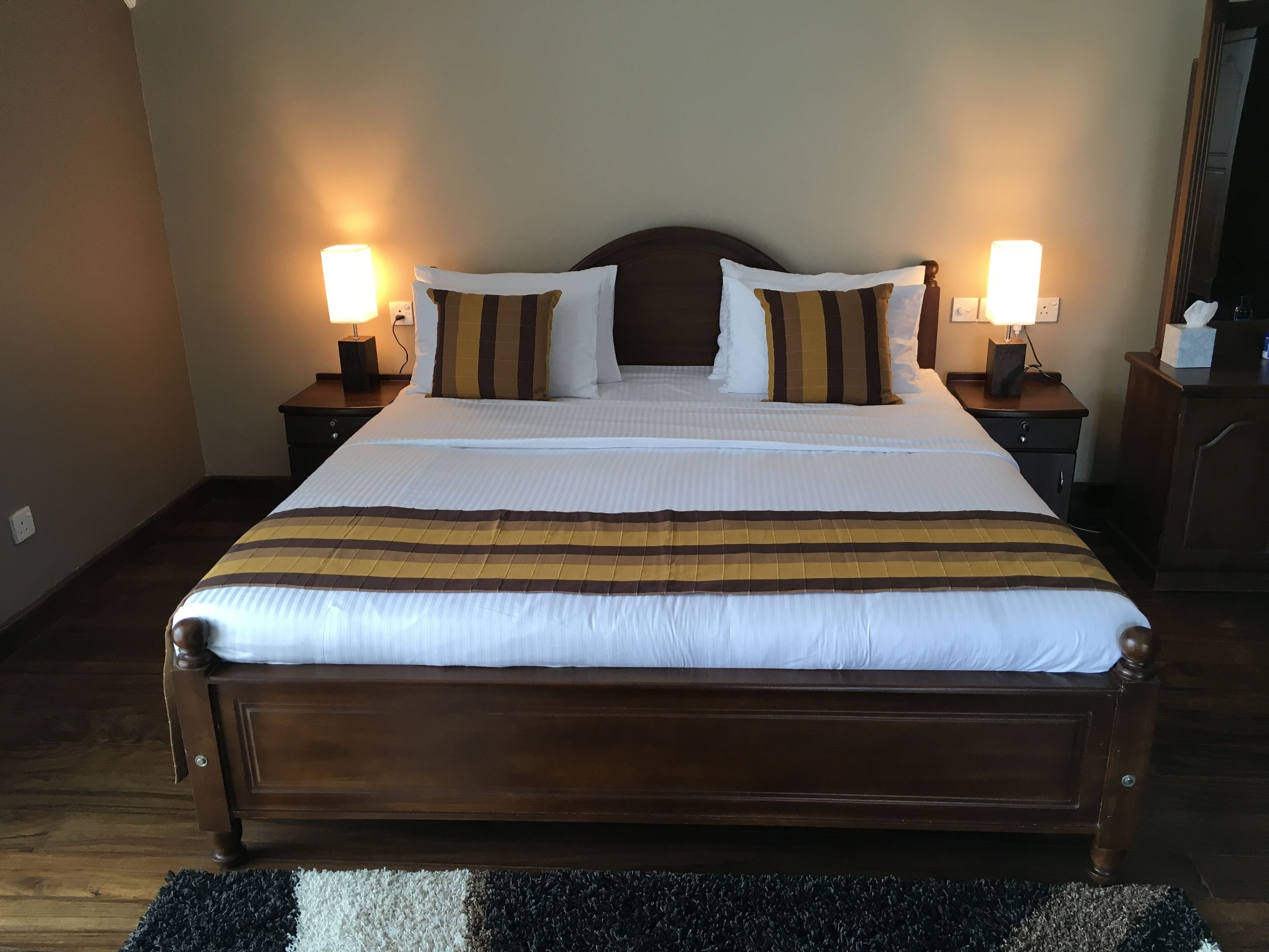 A large bed with a wooden headboard, two bedside tables with lamps, and a black and white rug.