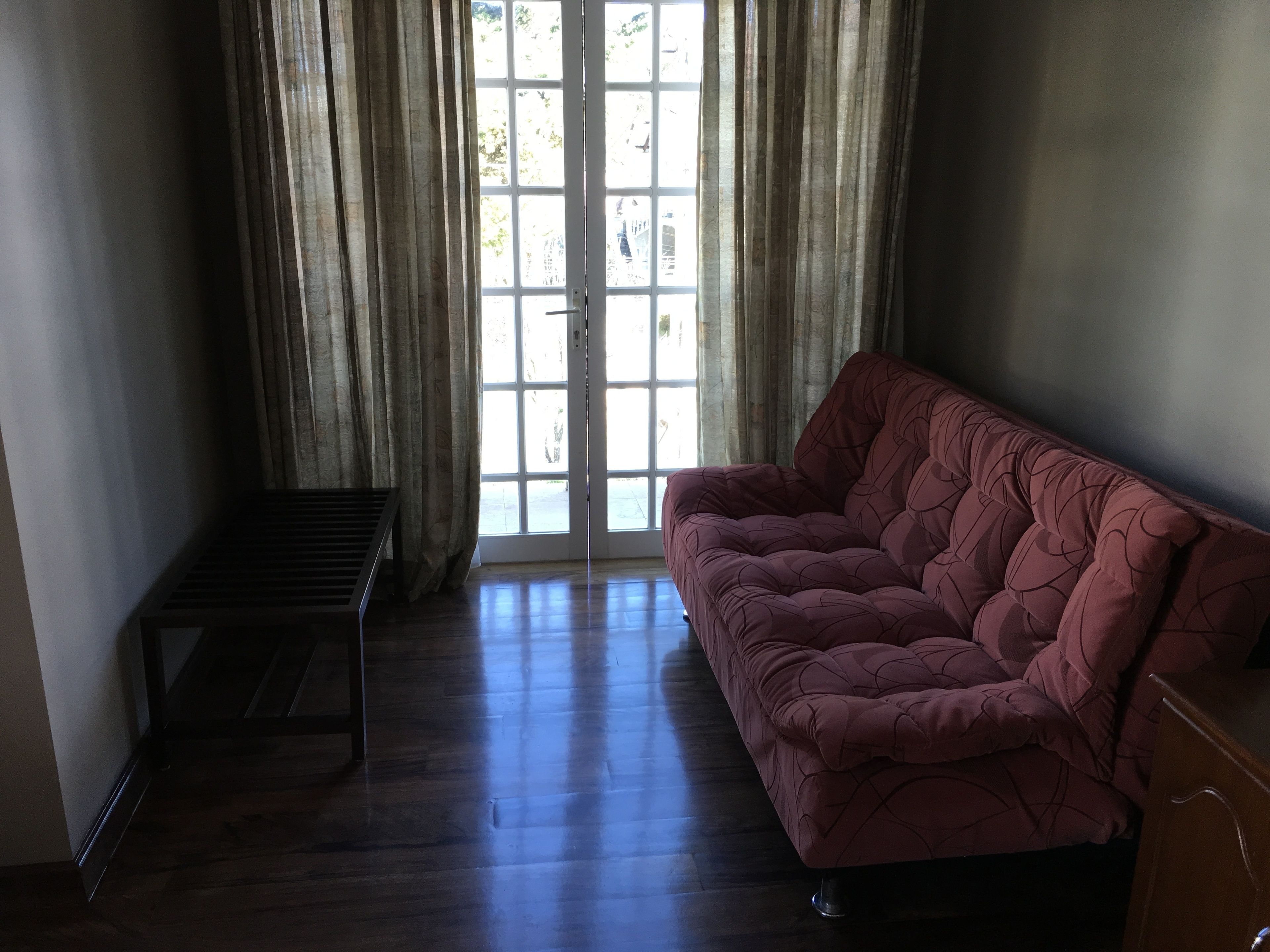 A room with a wooden floor, a sofa, a small table, and a door with curtains.