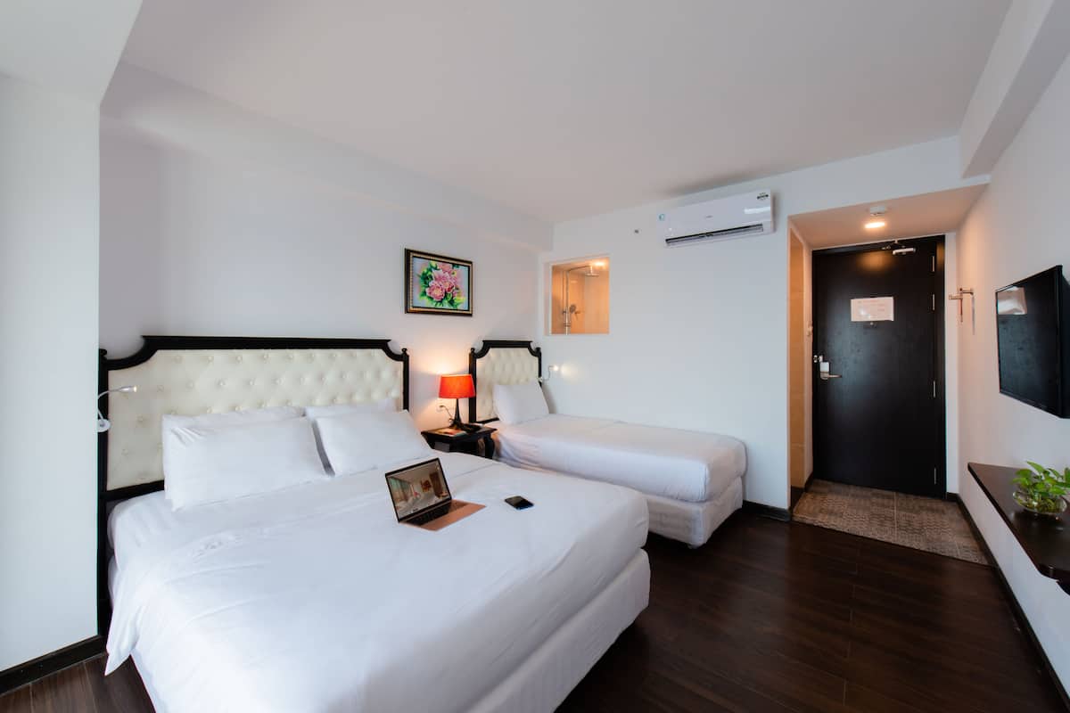 A hotel room with two beds, a desk with a laptop, a TV, and a painting on the wall.