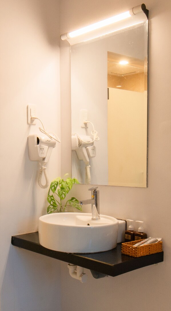 Une salle de bain avec un lavabo rond, un miroir, un sèche-cheveux et une plante.