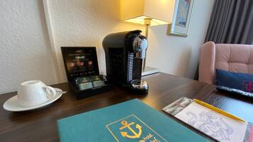 Ein Hotelzimmer mit Kaffeemaschine, einer Kaffeetasse, einer Auswahl an Kaffeekapseln, einer Fernbedienung und einem Buch mit Anker-Logo.