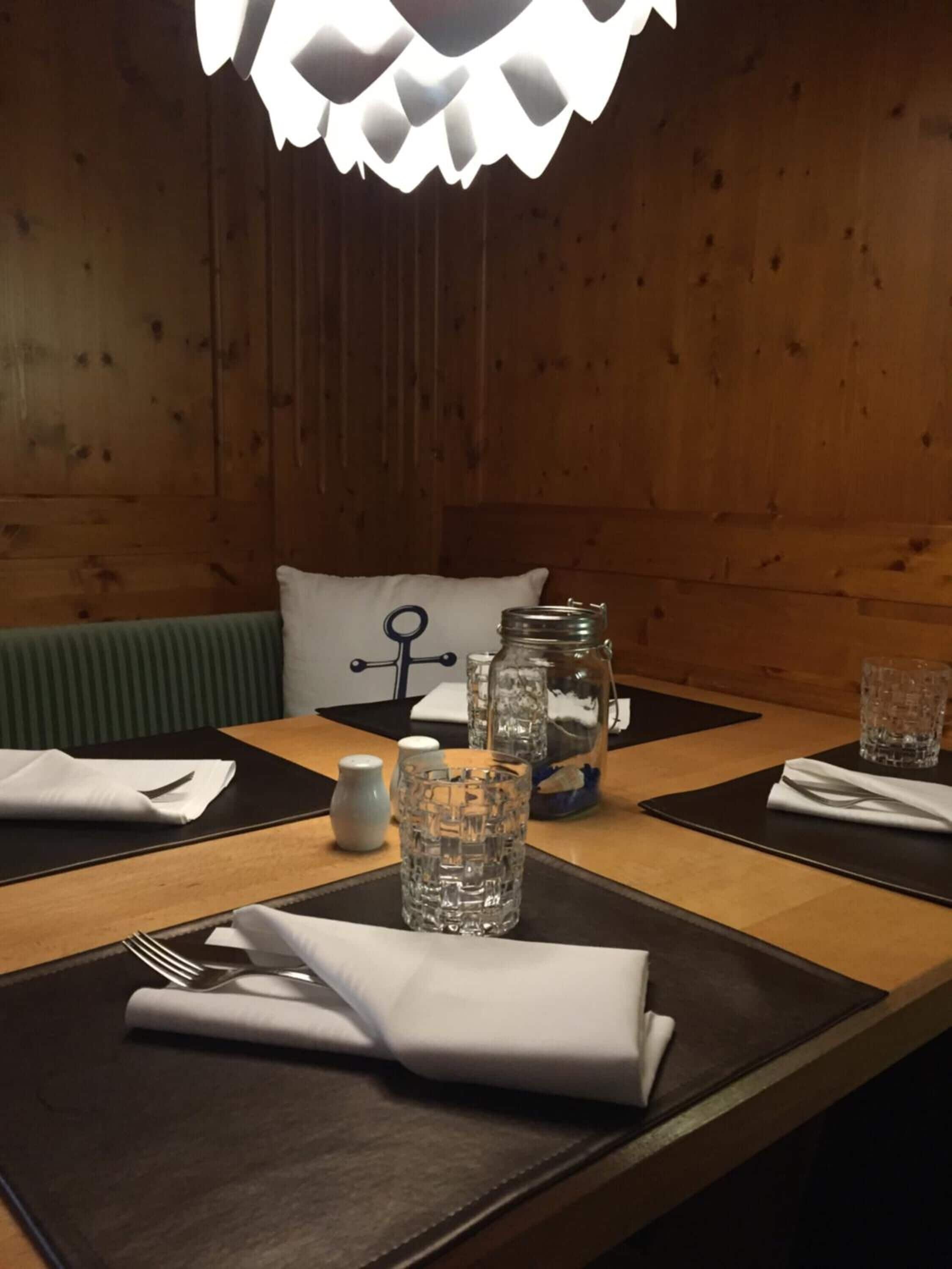 Une table à manger est dressée avec un verre, un bocal et une bouteille. On aperçoit en arrière-plan un mur en bois et un banc.